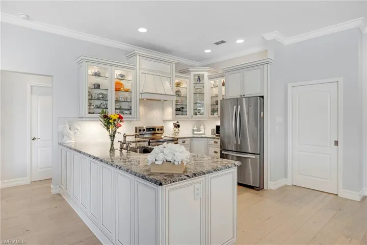 Kitchen with ornamental molding, light hardwood / wood-style flooring, stainless steel appliances, backsplash, and custom exhaust hood