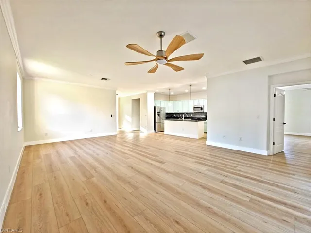 Unfurnished living room featuring crown molding, a ceiling fan, and light wood-style flooring