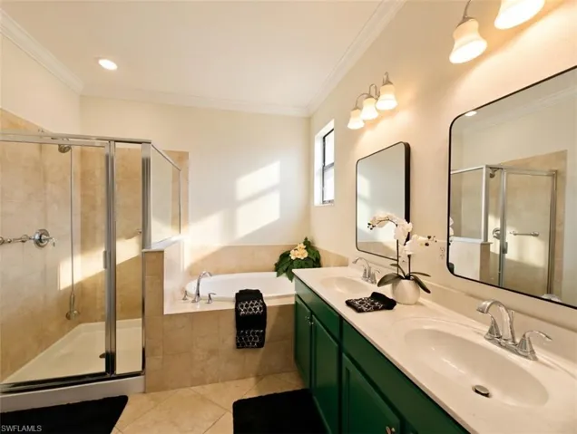 Bathroom featuring double vanity, a garden tub, a shower stall, ornamental molding, and light tile patterned flooring