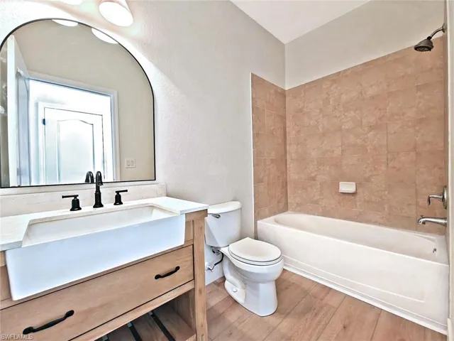 Full bathroom with shower / bathtub combination, vanity, light wood-style floors, and a textured wall