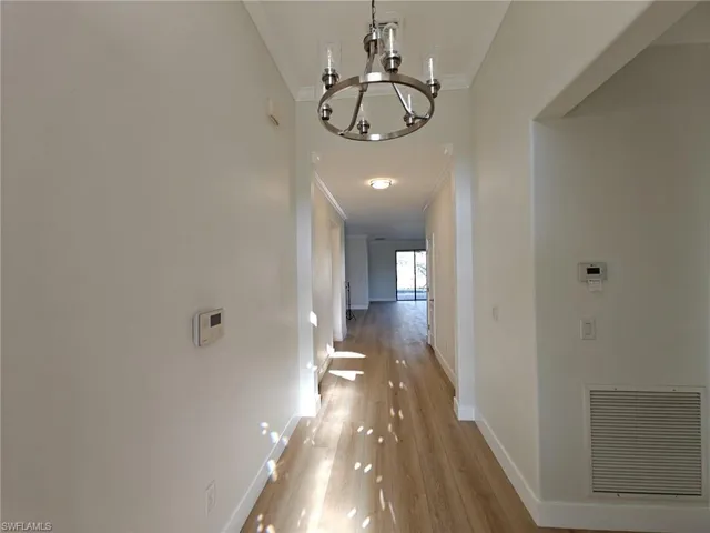 Corridor with ornamental molding, a chandelier, and light wood-style flooring