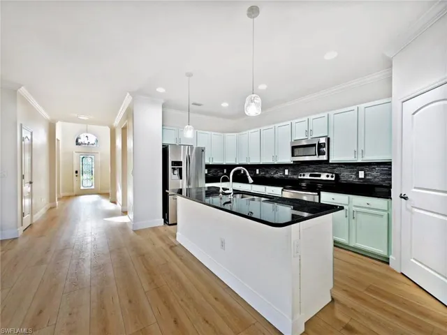Kitchen with tasteful backsplash, ornamental molding, stainless steel appliances, an island with sink, and light wood finished floors