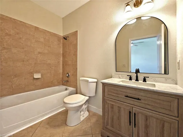 Bathroom featuring a textured wall, washtub / shower combination, vanity, and light tile patterned floors
