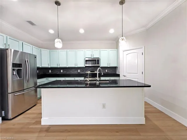 Kitchen featuring stainless steel appliances, tasteful backsplash, hanging light fixtures, crown molding, and light wood-style flooring