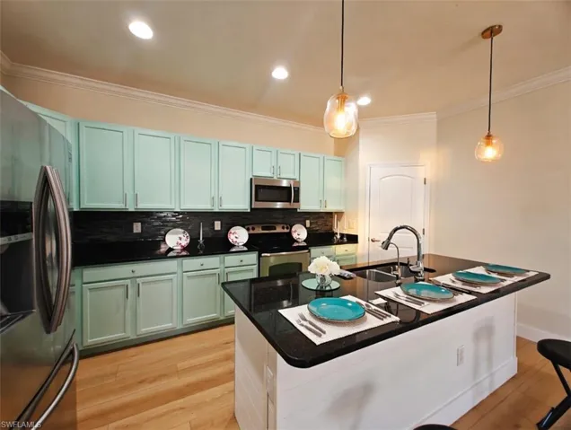 Kitchen featuring stainless steel appliances, crown molding, light wood-style floors, a kitchen island with sink, and backsplash