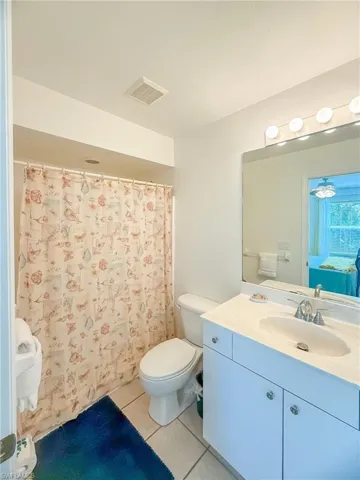 Bathroom featuring toilet, tile patterned floors, vanity, visible vents, and a shower with curtain