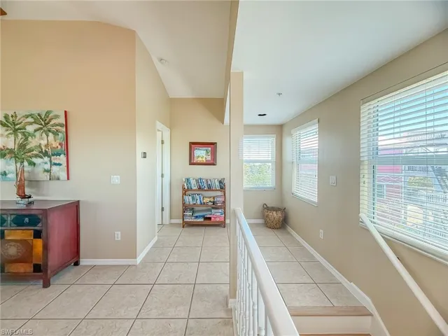 Corridor with lofted ceiling, light tile patterned floors, baseboards, and an upstairs landing