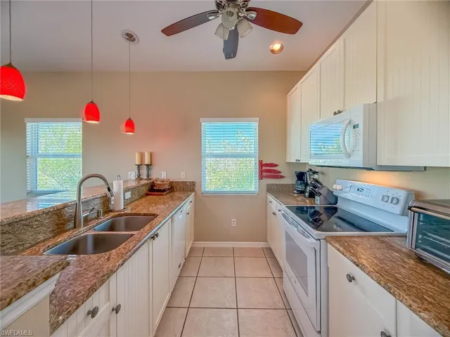 Kitchen featuring light tile patterned floors, white appliances, a sink, and a healthy amount of sunlight
