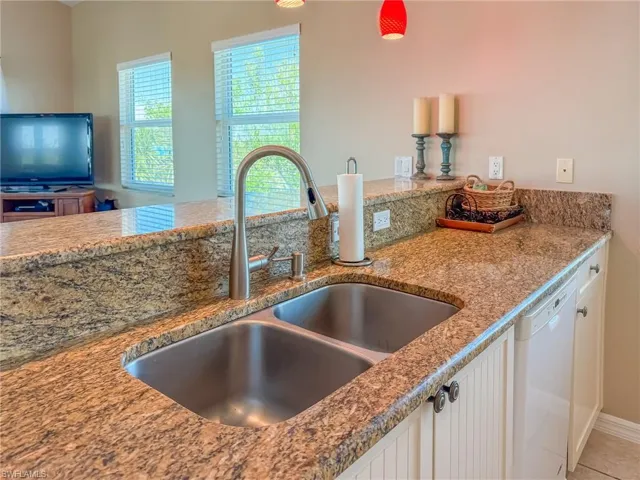 Kitchen featuring white dishwasher, a sink, white cabinetry, and light stone countertops
