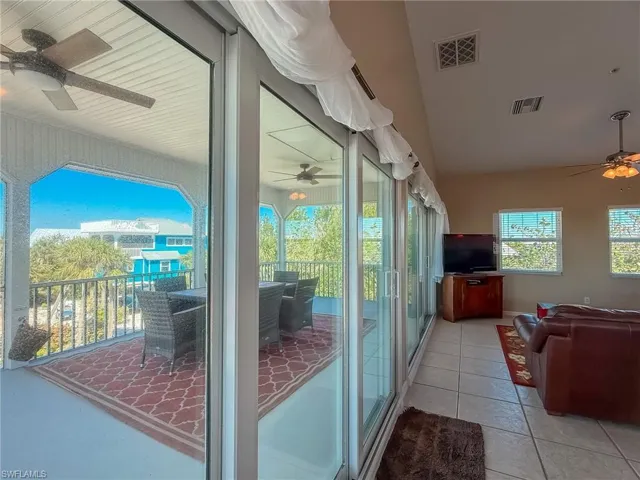 Doorway to outside with lofted ceiling, light tile patterned floors, visible vents, and a ceiling fan