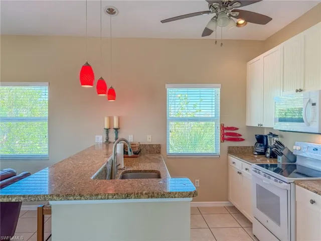 Kitchen with light tile patterned floors, white cabinetry, a sink, white appliances, and a peninsula
