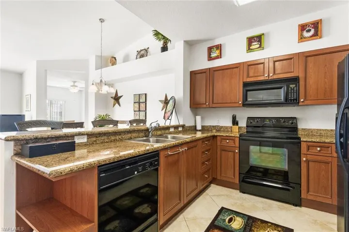 Kitchen featuring kitchen peninsula, vaulted ceiling, sink, black appliances, and decorative light fixtures