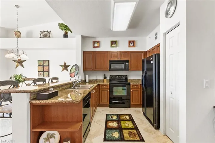 Kitchen with a kitchen breakfast bar, kitchen peninsula, decorative light fixtures, vaulted ceiling, and black appliances