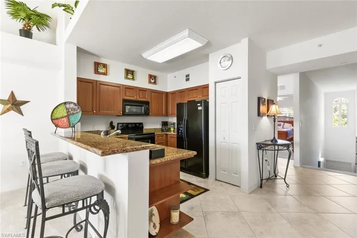 Kitchen with dark stone counters, black appliances, light tile patterned floors, a kitchen bar, and kitchen peninsula
