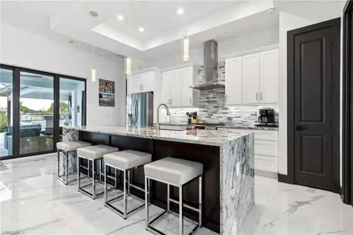 Kitchen with light marble finish floors, tasteful backsplash, white cabinetry, a kitchen breakfast bar, and hanging light fixtures