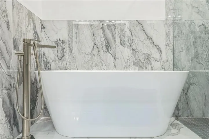 Bathroom with marble tiled flooring, a freestanding bath, and tile walls