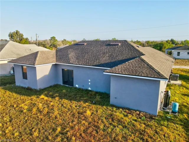 Rear view of property with stucco siding, a shingled roof, and a yard