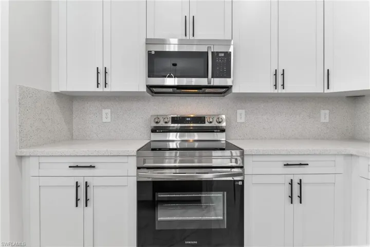 Kitchen featuring stainless steel appliances, light stone countertops, white cabinets, and decorative backsplash