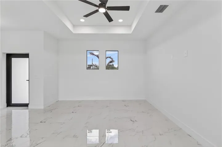 Spare room with a raised ceiling, a ceiling fan, light marble finish flooring, and recessed lighting