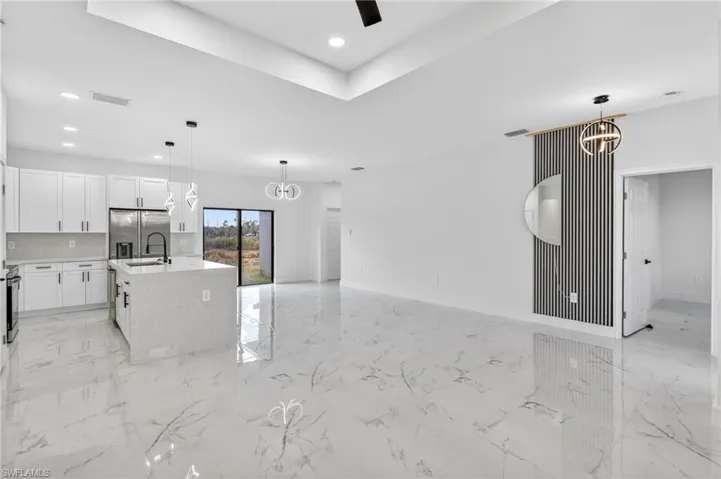 Kitchen featuring a chandelier, a kitchen island with sink, open floor plan, white cabinets, and light stone countertops