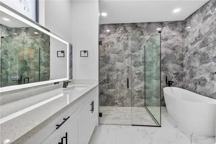 Bathroom with vanity, a freestanding bath, recessed lighting, a marble finish shower, and light marble finish flooring