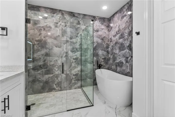 Bathroom featuring a marble finish shower, a freestanding tub, marble finish floors, tile walls, and recessed lighting