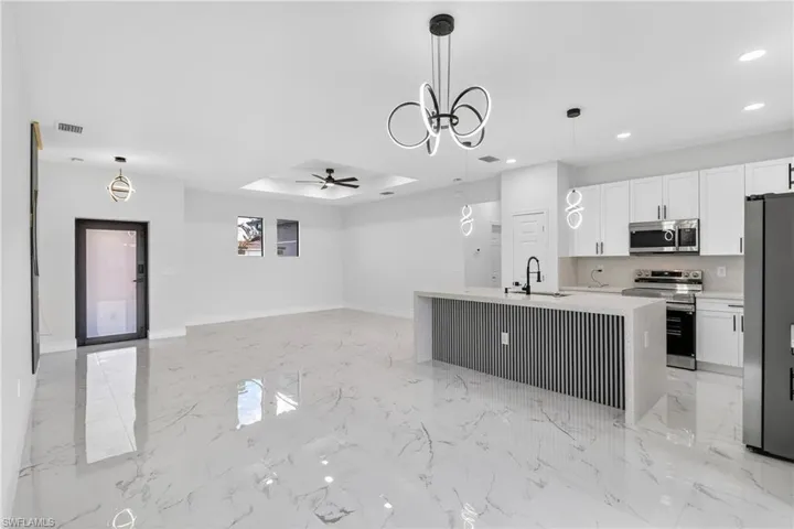 Kitchen featuring stainless steel appliances, open floor plan, ceiling fan, an island with sink, and white cabinets