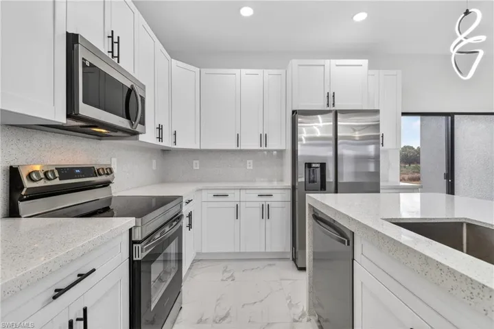 Kitchen featuring stainless steel appliances, light marble finish floors, white cabinetry, light stone countertops, and tasteful backsplash