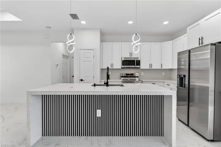 Kitchen featuring stainless steel appliances, light stone counters, white cabinets, and tasteful backsplash