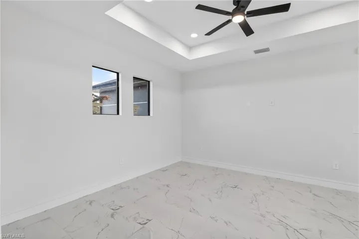 Empty room featuring a ceiling fan, light marble finish floors, a tray ceiling, and recessed lighting