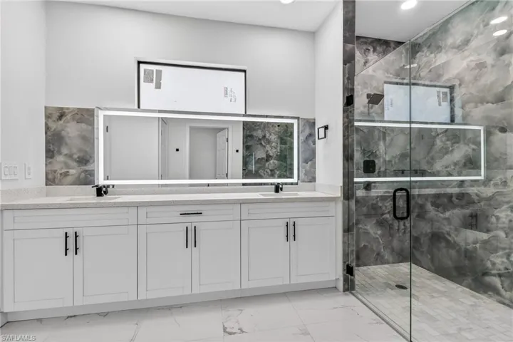 Full bathroom with double vanity, a marble finish shower, light marble finish floors, and recessed lighting