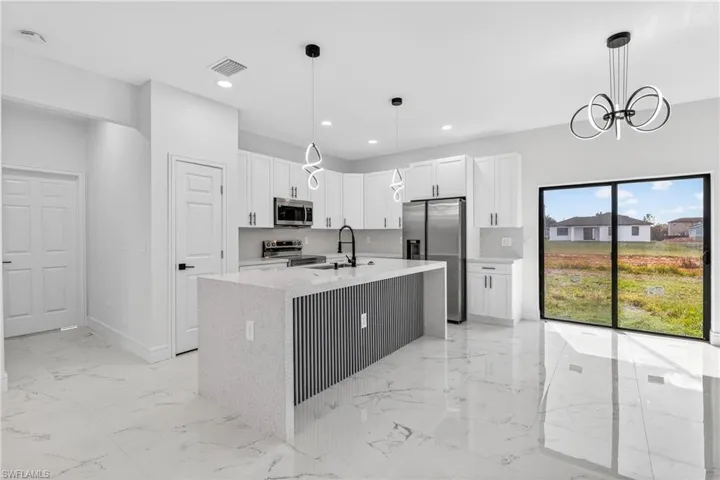 Kitchen with stainless steel appliances, white cabinets, light stone countertops, an island with sink, and hanging lights