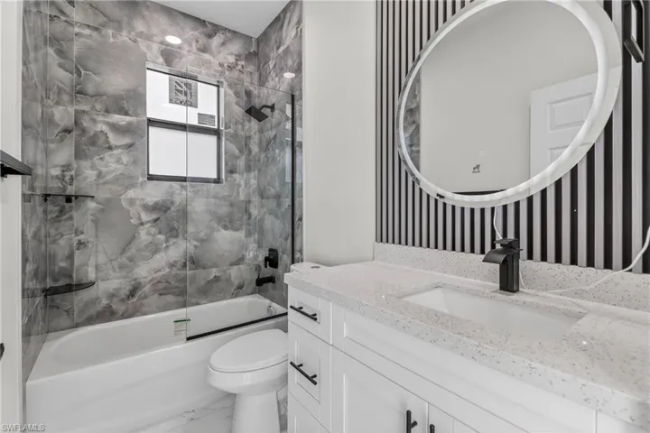 Bathroom featuring vanity, shower / bath combination with glass door, and wallpapered walls