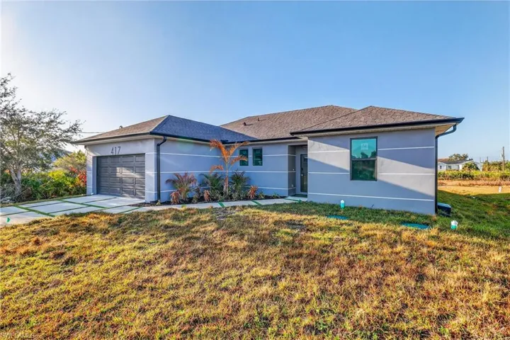 Ranch-style house with a front lawn, an attached garage, stucco siding, and driveway