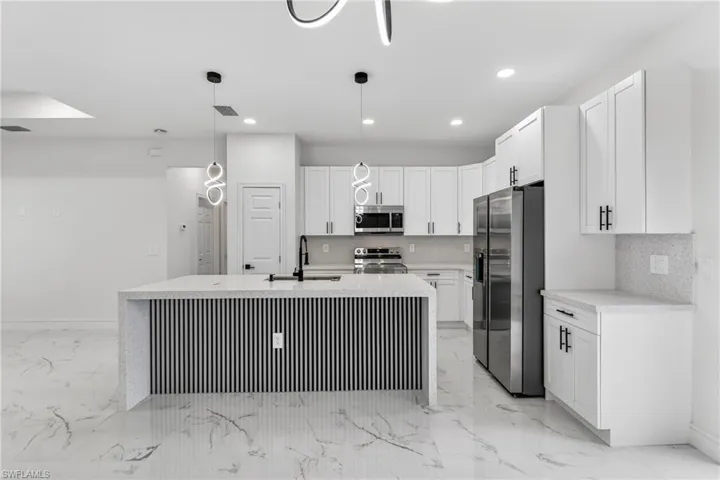 Kitchen with stainless steel appliances, backsplash, light stone countertops, white cabinetry, and decorative light fixtures