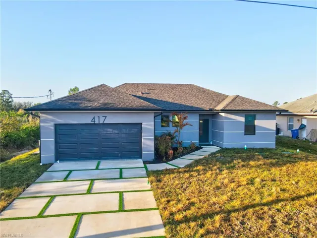 Ranch-style home with stucco siding, driveway, a garage, a front yard, and roof with shingles