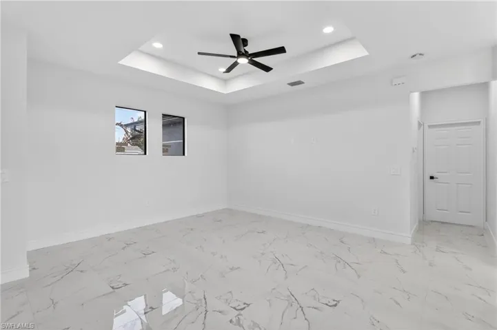 Spare room with a ceiling fan, a tray ceiling, recessed lighting, and light marble finish flooring