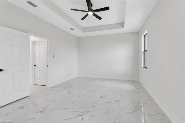 Spare room with a raised ceiling, a ceiling fan, and light marble finish floors