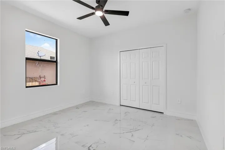 Unfurnished bedroom featuring a ceiling fan, light marble finish flooring, and a closet