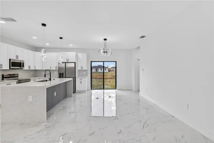 Kitchen with a chandelier, white cabinetry, stainless steel appliances, light stone countertops, and a kitchen island with sink