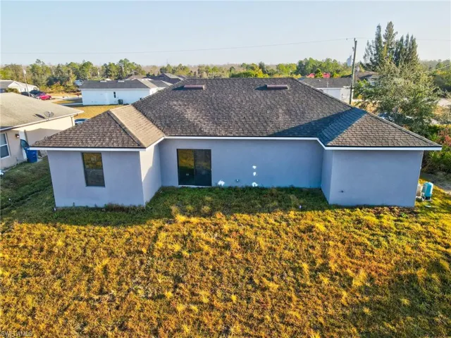 Rear view of property with stucco siding, a yard, and roof with shingles