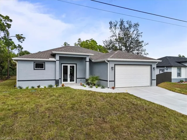 View of front facade with a front yard, stucco siding, concrete driveway, an attached garage, and french doors
