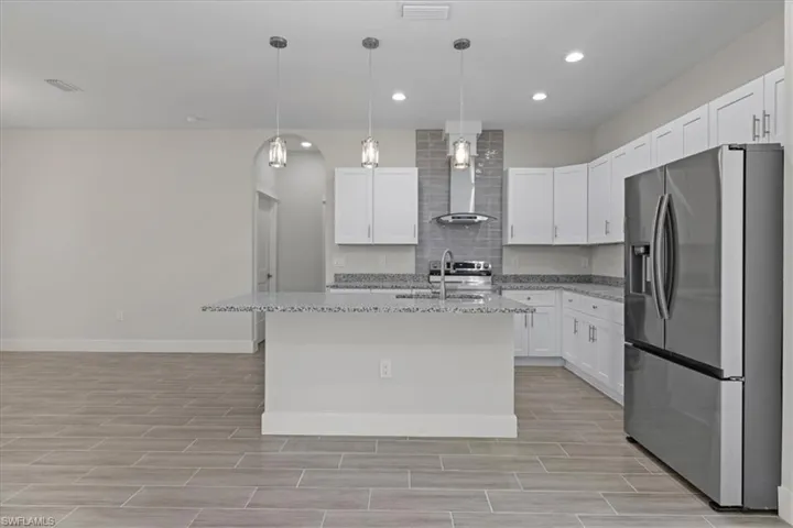 Kitchen featuring appliances with stainless steel finishes, light stone countertops, white cabinetry, hanging light fixtures, and recessed lighting
