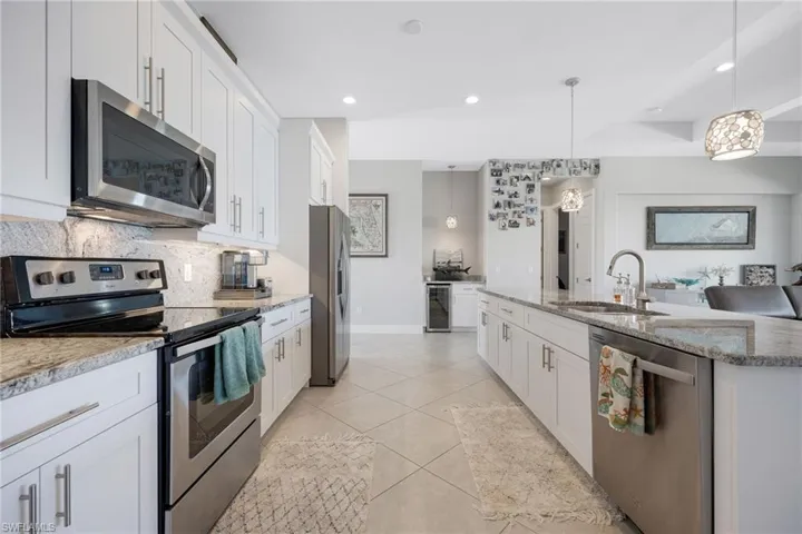 Kitchen featuring appliances with stainless steel finishes, white cabinets, light stone countertops, decorative light fixtures, and recessed lighting