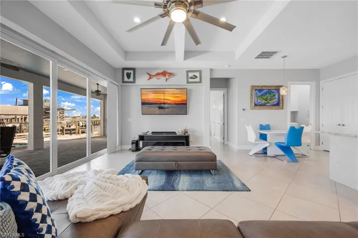 Living area featuring light tile patterned flooring, ceiling fan, a tray ceiling, and recessed lighting