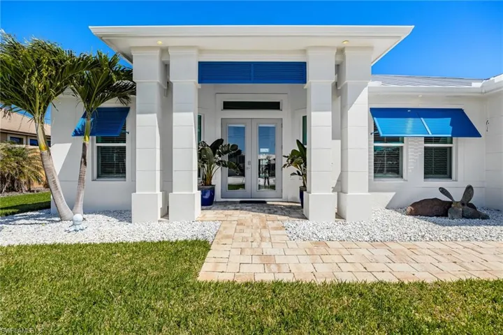 Property entrance with covered porch, french doors, stucco siding, and a lawn
