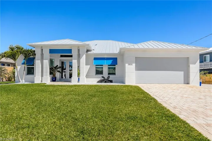 View of front of home with a standing seam roof, french doors, a front yard, a metal roof, and decorative driveway