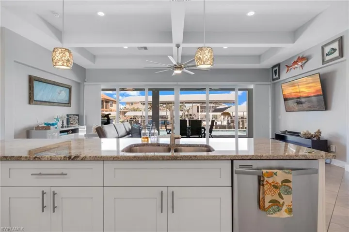 Kitchen featuring open floor plan, dishwasher, light stone counters, white cabinets, and coffered ceiling