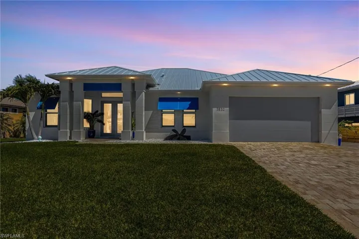 View of front of property featuring a standing seam roof, a metal roof, decorative driveway, a front lawn, and an attached garage