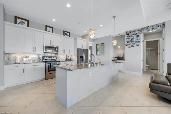 Kitchen with appliances with stainless steel finishes, pendant lighting, white cabinetry, light stone counters, and a center island with sink